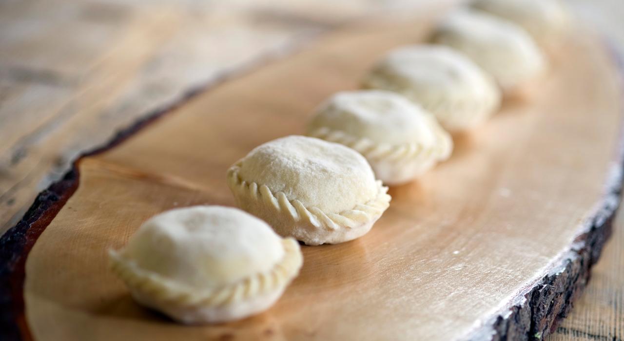 Kaernten_Kasnudel_Gerdl_roh Halbrunde Teigtaschen, die auf einem Holzbrett ausliegen, bereit zum Kochen oder Backen