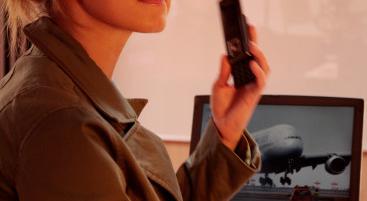 Eine Frau spricht am Telefon, im Hintergrund ist ein Bild eines Flugzeugs auf einem Laptop zu sehen