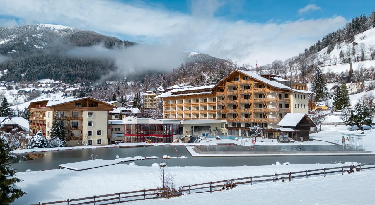Thermenwelt Hotel Pulverer in einer verschneiten Berglandschaft, umgeben von schneebedeckten Bäumen und Hügeln