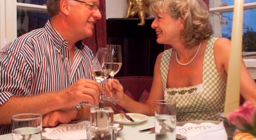 Ein Paar sitzt im Restaurant und stoßt mit zwei Gläsern Weißwein an