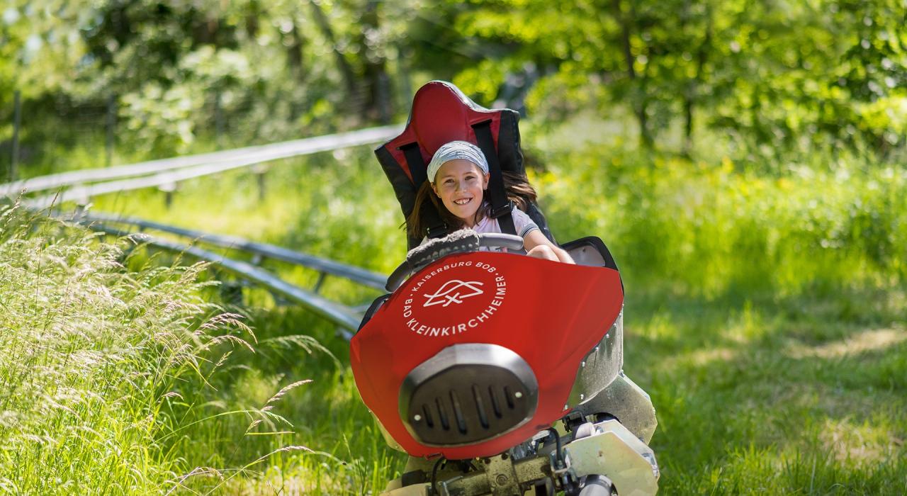 Ein kleines M&auml;dchen genie&szlig;t die Fahrt mit der Achterbahn in der Natur im Sommerurlaub in K&auml;rnten