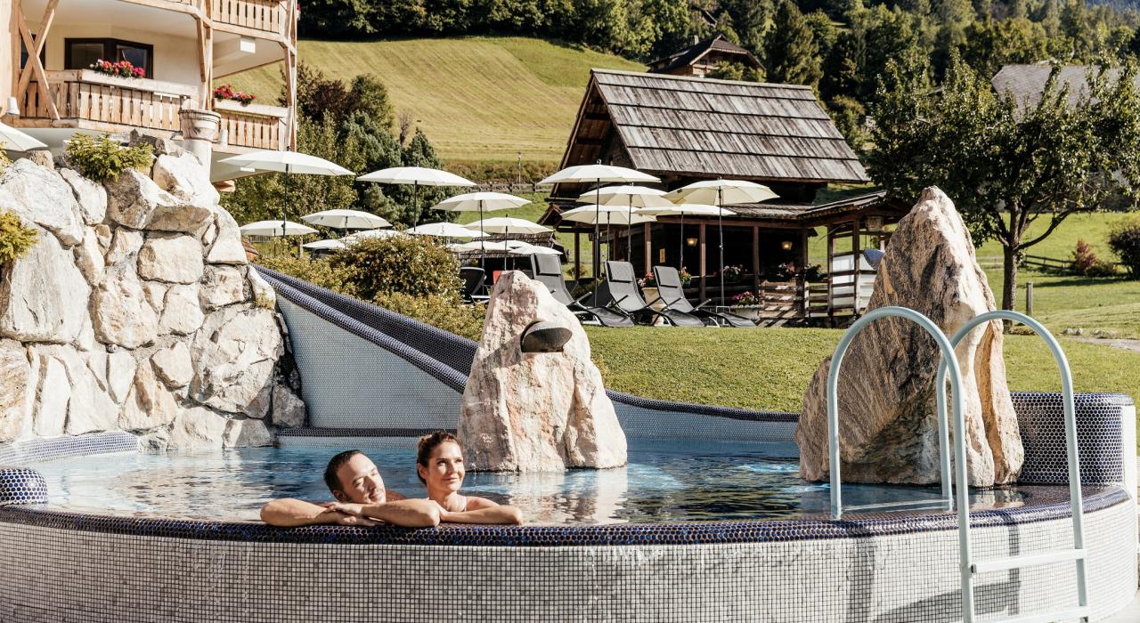 088A6575 Ein Paar entspannt in einem Außenpool, umgeben von Felsen und Liegestühlen mit Sonnenschirmen