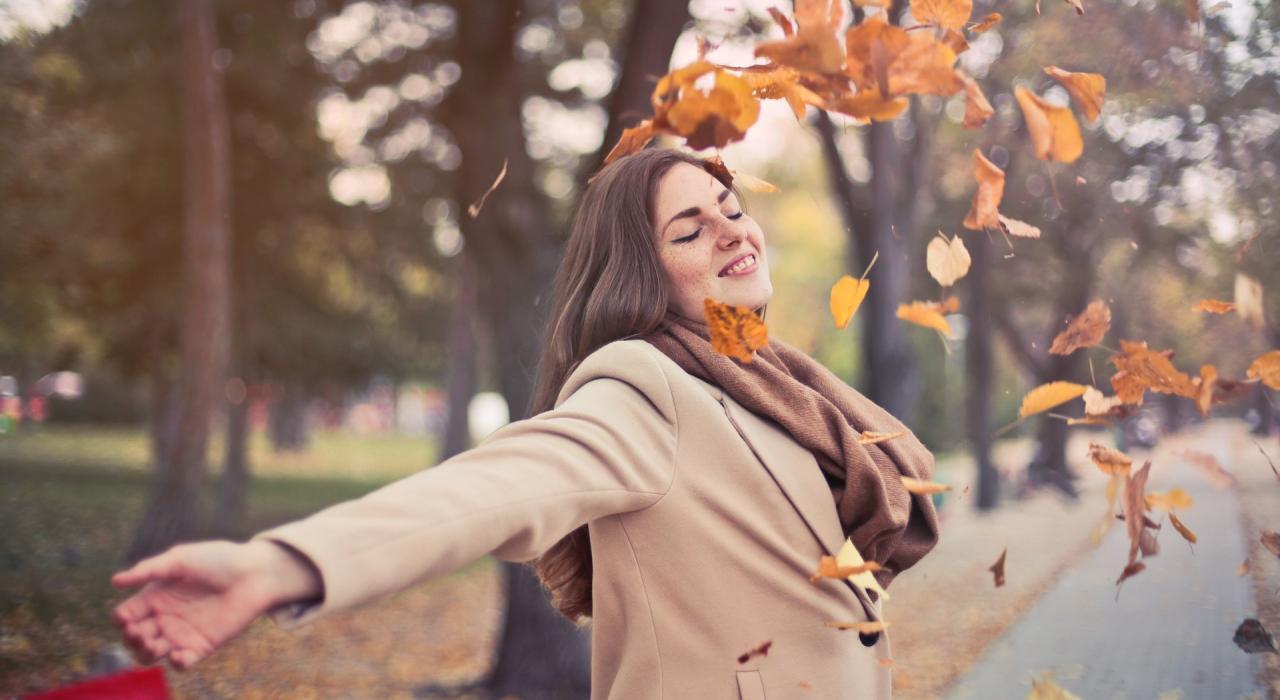 Frau schmeißt mit Herbstblättern um sich