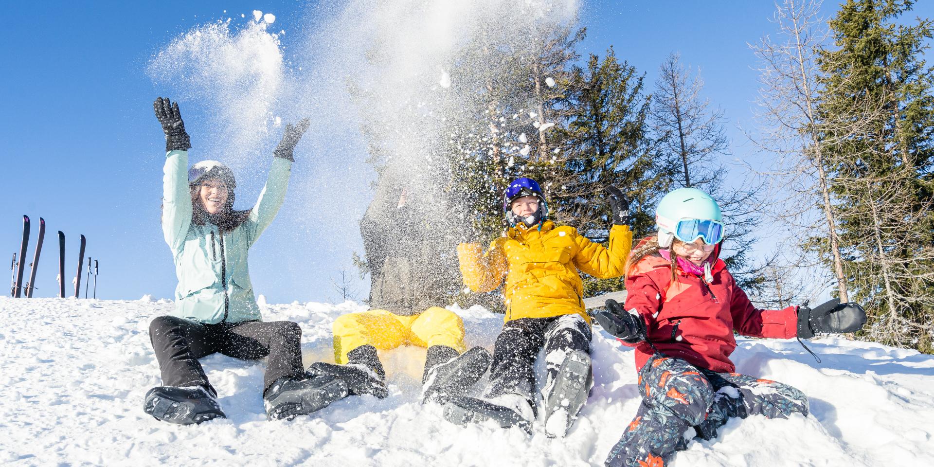 Skifahren_Familie_Bad Kleinkirchheim_Winter ©Mathias Prägant_MBN Tourismus(7) Eine Gruppe Menschen in Winterkleidung sitzt im Schnee und wirft lachend Schneebälle in die Luft