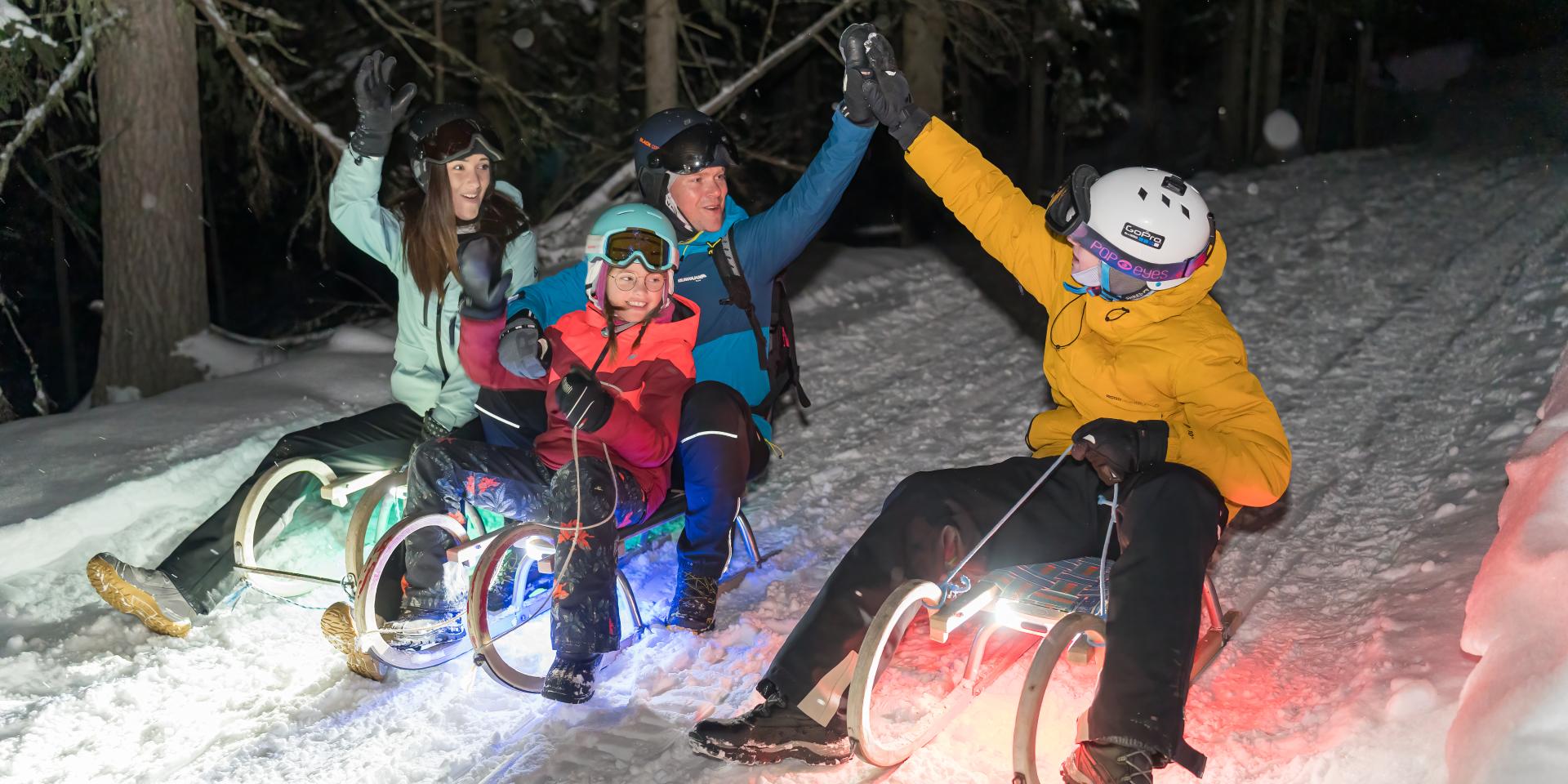 4 Menschen beim nächtlichen Schlittenfahren während ihres Winterurlaubs in unserem Familienhotel in Bad Kleinkirchheim
