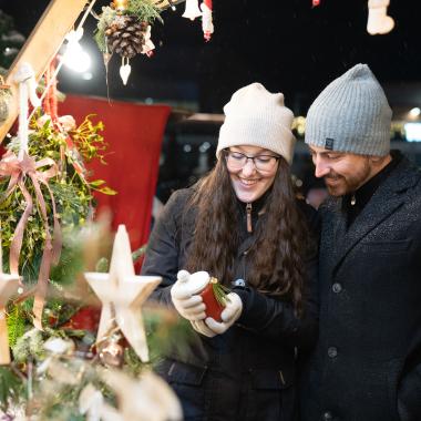 Ein Paar in Winterkleidung auf einem Weihnachtsmarkt betrachtet weihnachtliche Dekorationen
