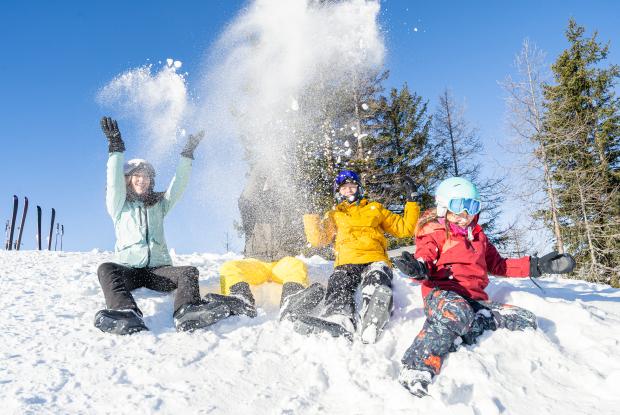 Skifahren_Familie_Bad Kleinkirchheim_Winter ©Mathias Prägant_MBN Tourismus(7) Eine Gruppe Menschen in Winterkleidung sitzt im Schnee und wirft lachend Schneebälle in die Luft