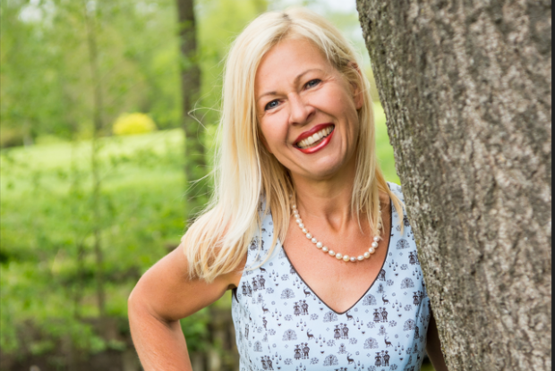 Fr__Mollner Frau Mollner lächelt in die Kamera und steht neben einem Baum