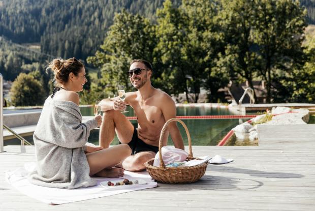 Ein Paar sitzt am Rand des Outdoor-Schwimmbads und stößt an