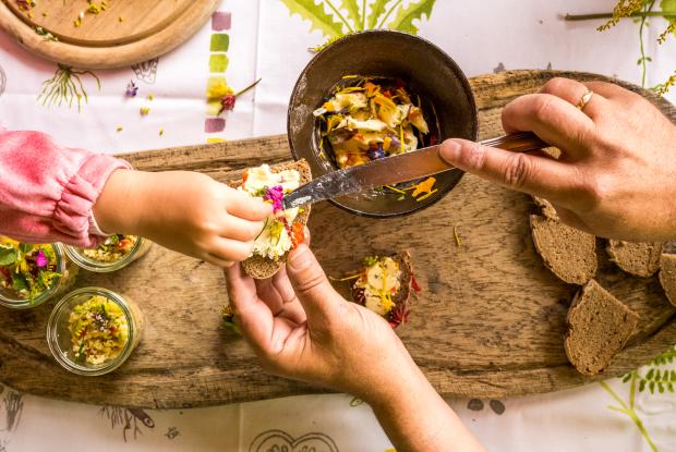 weissensee_sommer_barrierefrei-original_(f)_Michael-Stabentheiner_(c)_Kaernten-Werbung Eine Nahaufnahme zeigt, wie Hände gemeinsam Brot mit einem Aufstrich und essbaren Blüten dekorieren
