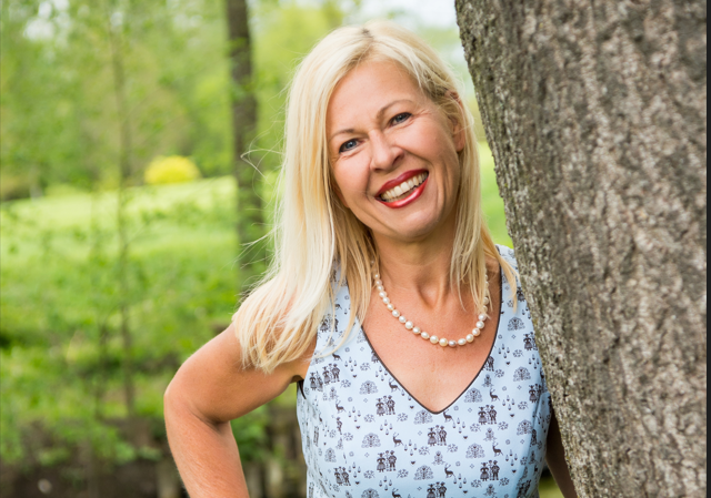 Fr__Mollner Frau Mollner lächelt in die Kamera und steht neben einem Baum